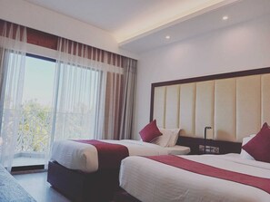 A hotel room with two beds, a large window with curtains, and a modern headboard.