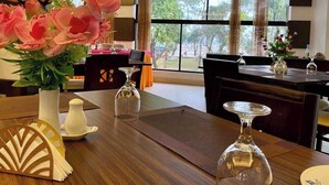 A dining area with a wooden table, clear glassware, and a bouquet of pink flowers. - Shada Pathor Hotel & Resort Sylhet  (Companiganj)
