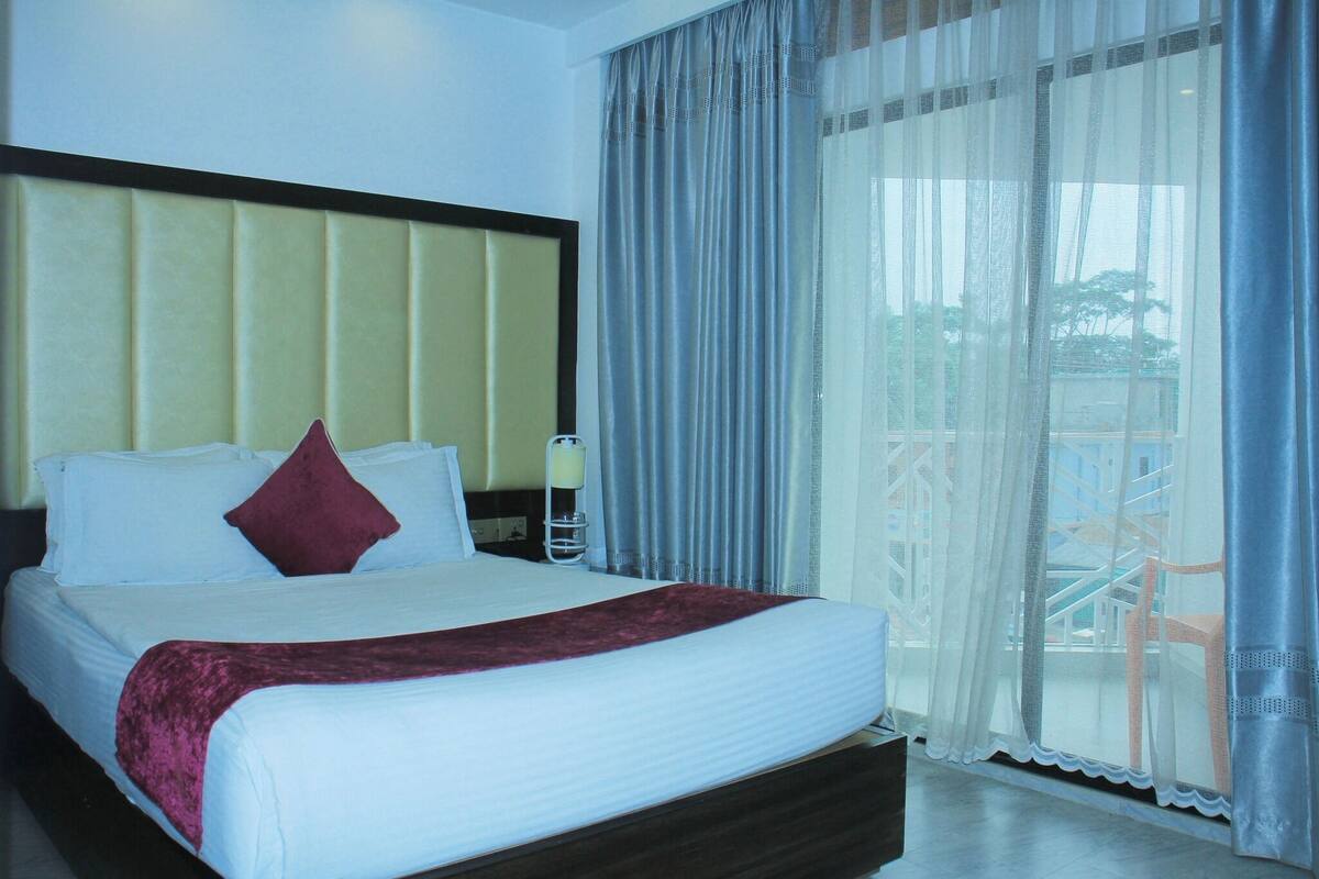 A hotel room with a large bed, a nightstand, and a window with sheer curtains.