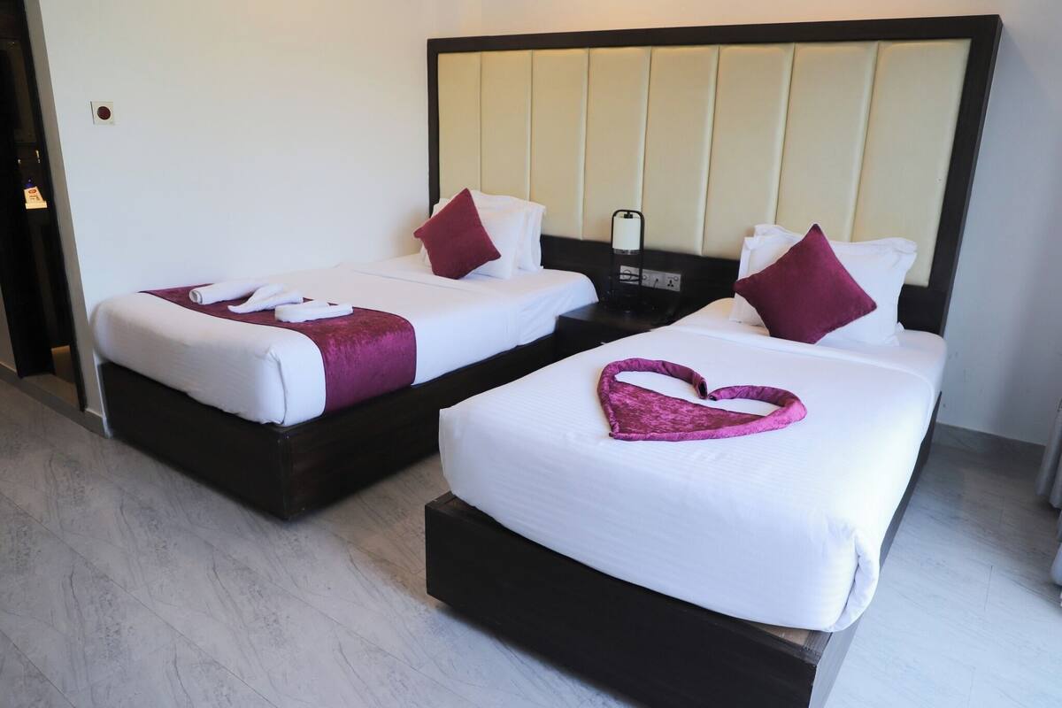 Two single beds with white linens and purple accents, a nightstand with a phone and lamp, and a modern room design.
