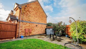 A brick house with a wooden fence, a patio with chairs, and a hose.
