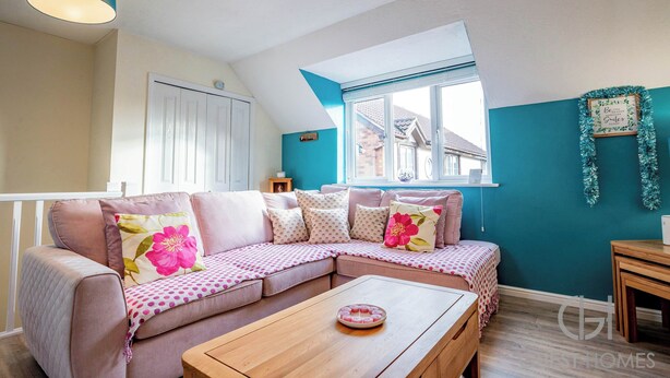 A cozy living room with a sectional sofa, a wooden coffee table, and a window with a view of houses.