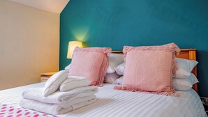 A neatly made bed with pink pillows and folded towels, a wooden nightstand with a lamp, and a teal accent wall.