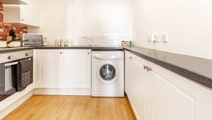 A compact kitchen with white cabinetry, a built-in oven, a washing machine, and a microwave. - Host & Stay | Flat 3 Club Chambers (Great Malvern)