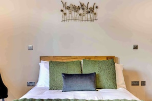 A bedroom with a wooden headboard, green and white bedding, and a wall-mounted decorative piece above the bed.