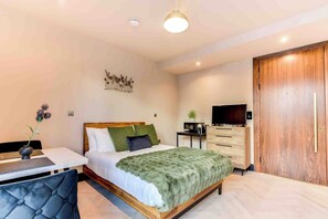 Ein modernes Schlafzimmer mit Bett, Nachttisch, Fernseher, Kleiderschrank und einem kleinen Schreibtisch mit Stuhl.