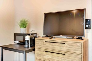 Een moderne kamer met een flatscreen televisie aan de muur, een koffieapparaat, een magnetron en een houten kast met lades.