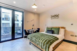 Quarto moderno com cama grande, escrivaninha e porta de vidro deslizante para área externa.