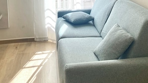 A room with a grey sofa, a window with sheer curtains, and a radiator on the wall. - HoneyComb GuestHouse (Rome)