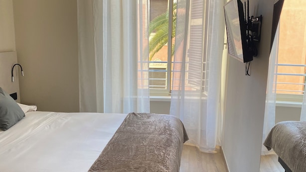 A hotel room with a bed, a sofa, a small table, and a TV mounted on the wall. - HoneyComb GuestHouse (Rome)