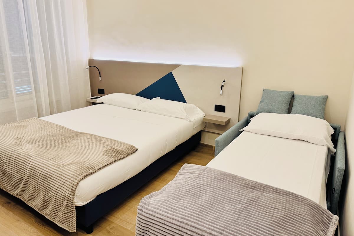 A hotel room with two beds, a bedside table, a nightstand, and a window with curtains.