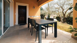An outdoor patio with a table and chairs, a door, and a view of trees and a building in the background. - Villa Syrah - private pool and terrace (Saint-Maurice-d’Ardèche)