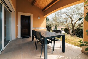 Eine Terrass mit Tisch und Stühlen, einer Tür und Blick auf Bäume sowie ein Gebäude im Hintergrund.