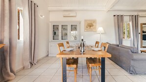 A dining area with a wooden table, chairs, and a sofa. There is a cabinet with glass doors and a lamp on the wall. - Villa Syrah - private pool and terrace (Saint-Maurice-d’Ardèche)