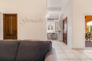 Ein Wohnzimmer mit grauem Sofa, einer Holztür und einer im Hintergrund sichtbaren Küche.