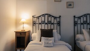 Un dormitorio con dos camas, una mesita de noche con lámpara y cuadros en la pared.