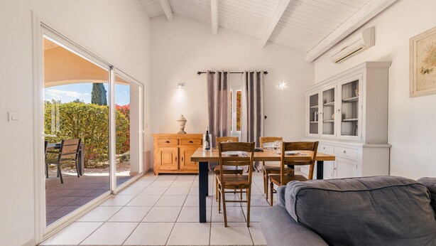 Una habitación con una mesa de comedor, sillas, un sofá, un armario y un gran ventanal corredizo que da a un espacio exterior.