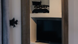Una habitación con un espejo de marco de madera que refleja un televisor y estantes con un objeto decorativo y un vaso.