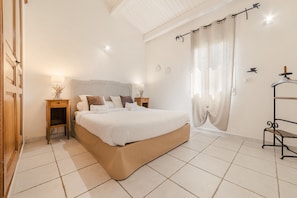 Un dormitorio con cama, mesitas de noche, un banco y una ventana con cortinas.