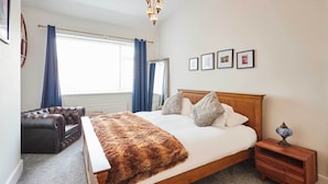 A bedroom with a wooden bed, a nightstand, a leather armchair, and a large window with curtains.