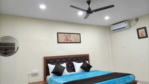 A bedroom with a bed, a ceiling fan, an air conditioning unit, a wall-mounted mirror, and a framed picture.