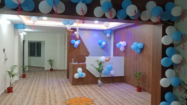 A reception area with a wooden reception desk, blue and white balloons, potted plants, and a wooden floor.