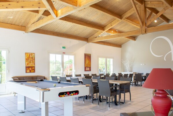 A spacious indoor area with a pool table, multiple dining tables, and chairs.