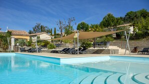 Une piscine aux eaux cristallines, dotée de chaises longues et d’un espace ombragé, le tout entouré d’un mur de pierre et de verdure.
