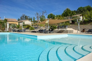 Piscina cristalina con tumbonas y una zona con sombra, rodeada de un muro de piedra y vegetación.