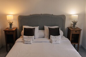 A neatly made bed with white linens and two decorative pillows, flanked by two bedside tables with lamps and small decorative items.