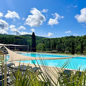 Ein Swimmingpool mit Liegestühlen und Blick auf grüne Hügel.