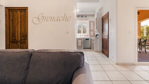 Un salon avec un canapé gris, une porte en bois et une cuisine visible au fond.