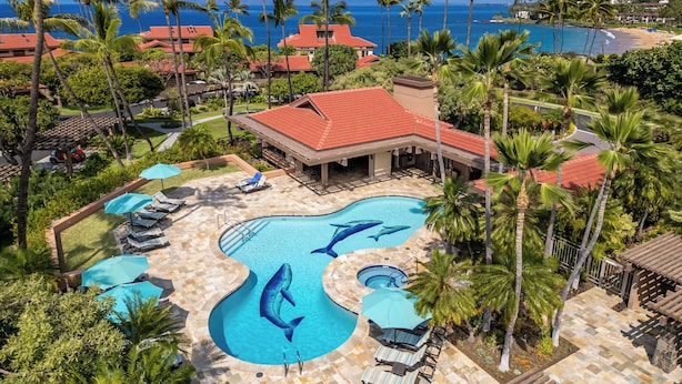 A resort with a swimming pool featuring dolphin designs, surrounded by palm trees and a view of the ocean. - Wailea Point Executive 2 Bedroom/3 Bath Oceanview Vacation Home (Wailea)