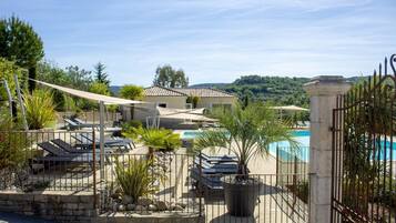 Un área de piscina con sillones de descanso, una pared de piedra y vistas a una casa y colinas.