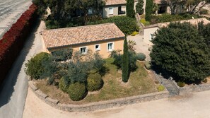 A single-story building with a tiled roof, surrounded by a well-maintained garden with various shrubs and a paved driveway.
