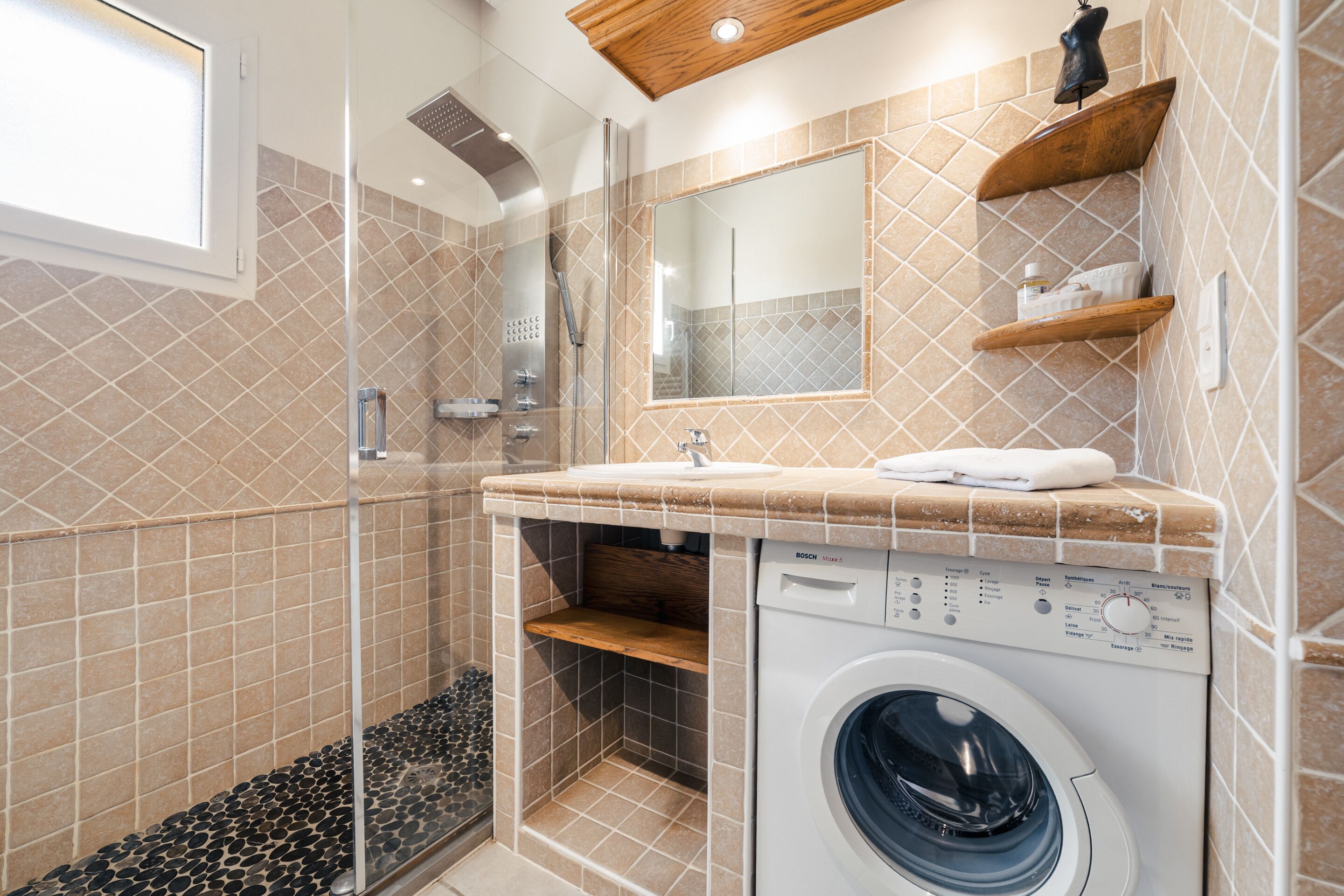 A bathroom with a washing machine, a shower, and a mirror.