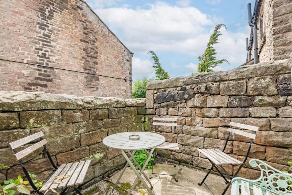 A stone wall with a round table and two wooden benches.