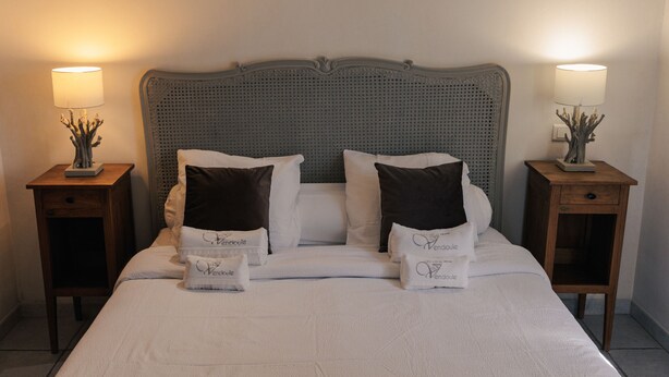 A neatly made bed with white linens and two decorative pillows, flanked by two bedside tables with lamps and small decorative items. - Villa Merlot - private terrace and garden (Saint-Maurice-d’Ardèche)