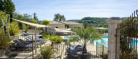 A pool area with lounge chairs, a stone wall, and a view of a house and hills.