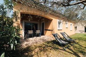 Ein Gebäude mit einer überdachten Terrasse, Sitzgelegenheiten im Freien und einem Rasen.