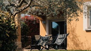 A building with a beige exterior, a window, and a patio area with two lounge chairs and a table.