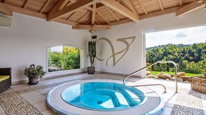 Un bain à remous avec vue sur une forêt, un grand mur orné d’un motif décoratif et un plafond en bois.