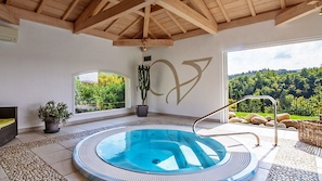A hot tub with a view of a forest, a large wall with a design, and a wooden ceiling.