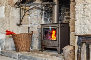 A stone fireplace with a metal stove, a wicker basket, and a wooden table. - Host & Stay | Old Hall - Middle Mayfield (Middle Mayfield)