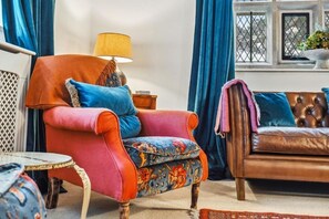 A cozy living room with a vibrant orange armchair, a patterned blue sofa, and a small round table.