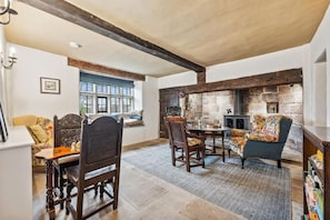 Un coin repas chaleureux avec une table et des chaises en bois, une cheminée en pierre et une fenêtre agrémentée de volets bleus.