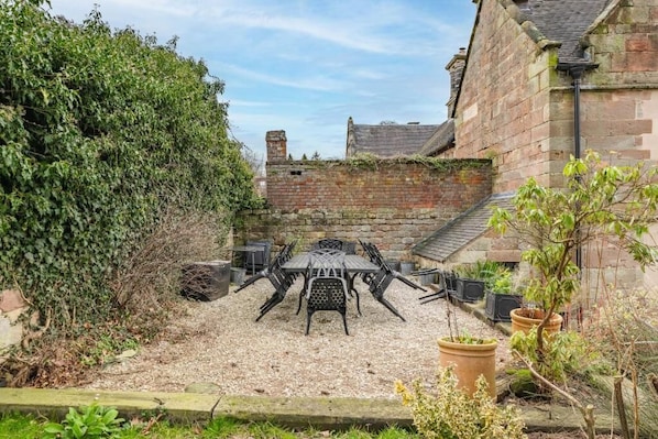 Une terrasse avec une table et des chaises, entourée d’un mur de pierre et de verdure.