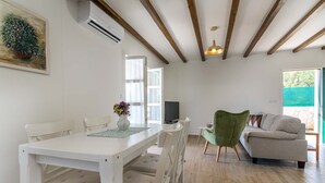 A room with a white dining table, chairs, a green armchair, a sofa, and a TV.