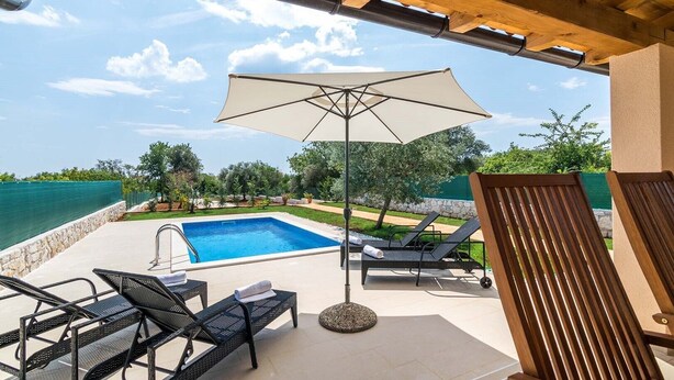 A pool area with lounge chairs and an umbrella, overlooking a body of water.