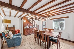 A dining area with a wooden table and chairs, a staircase, and a cozy blue armchair.